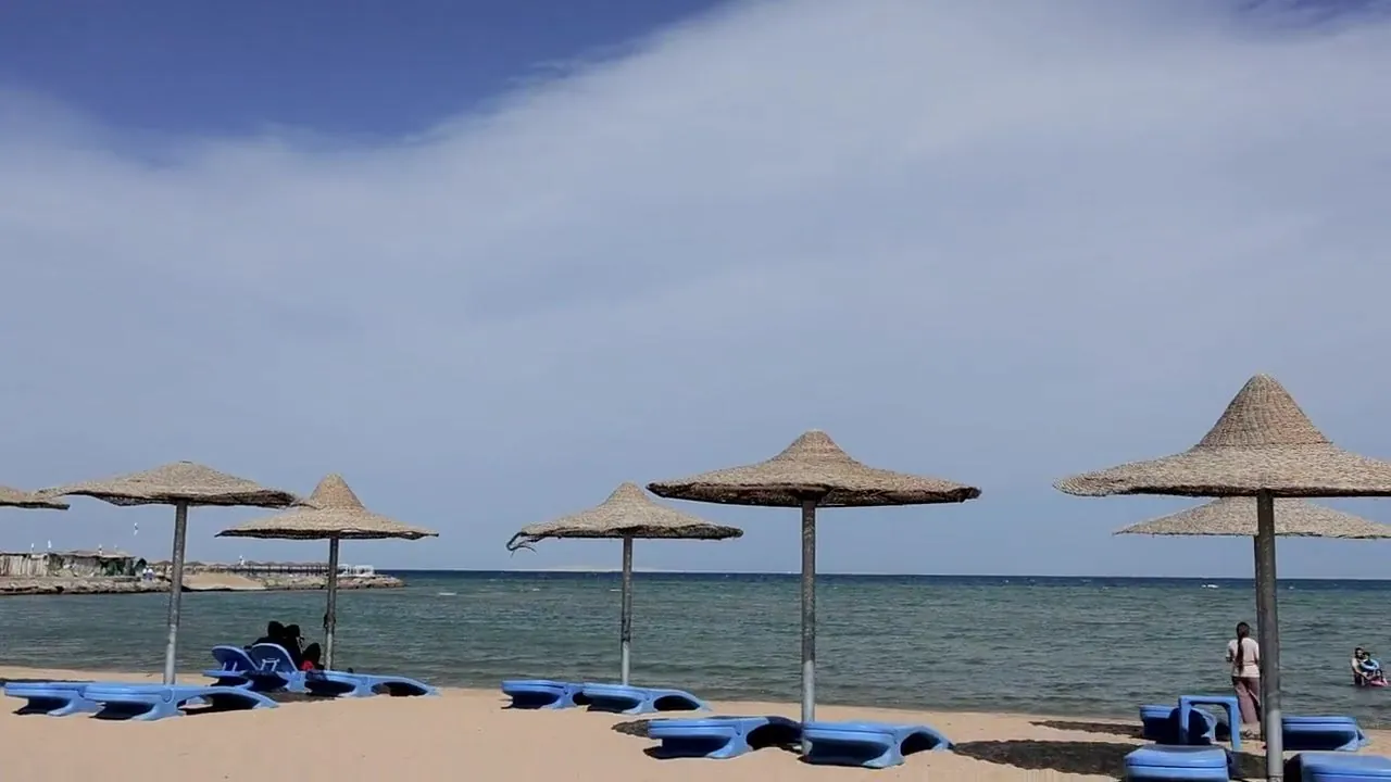 Straw umbrellas and blue sunbeds on the sand, with the Red Sea beyond