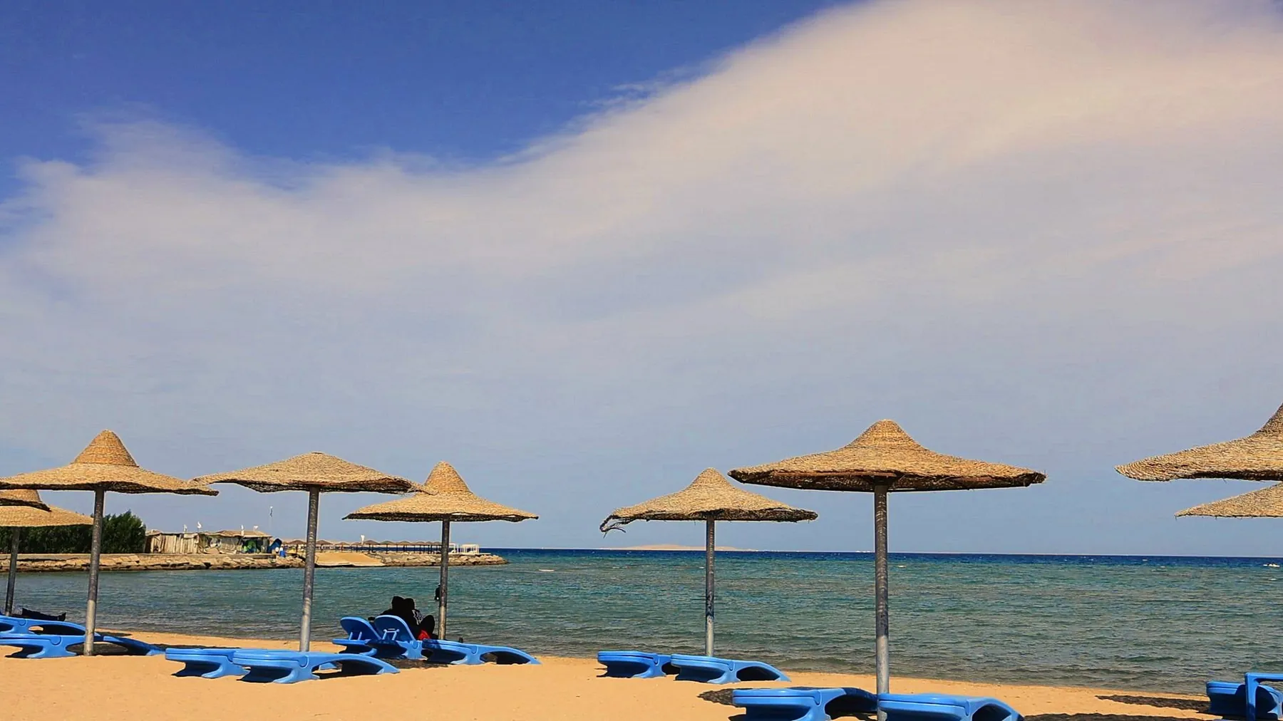 Strohschirme und blaue Sonnenliegen am Meer unter weitem Himmel