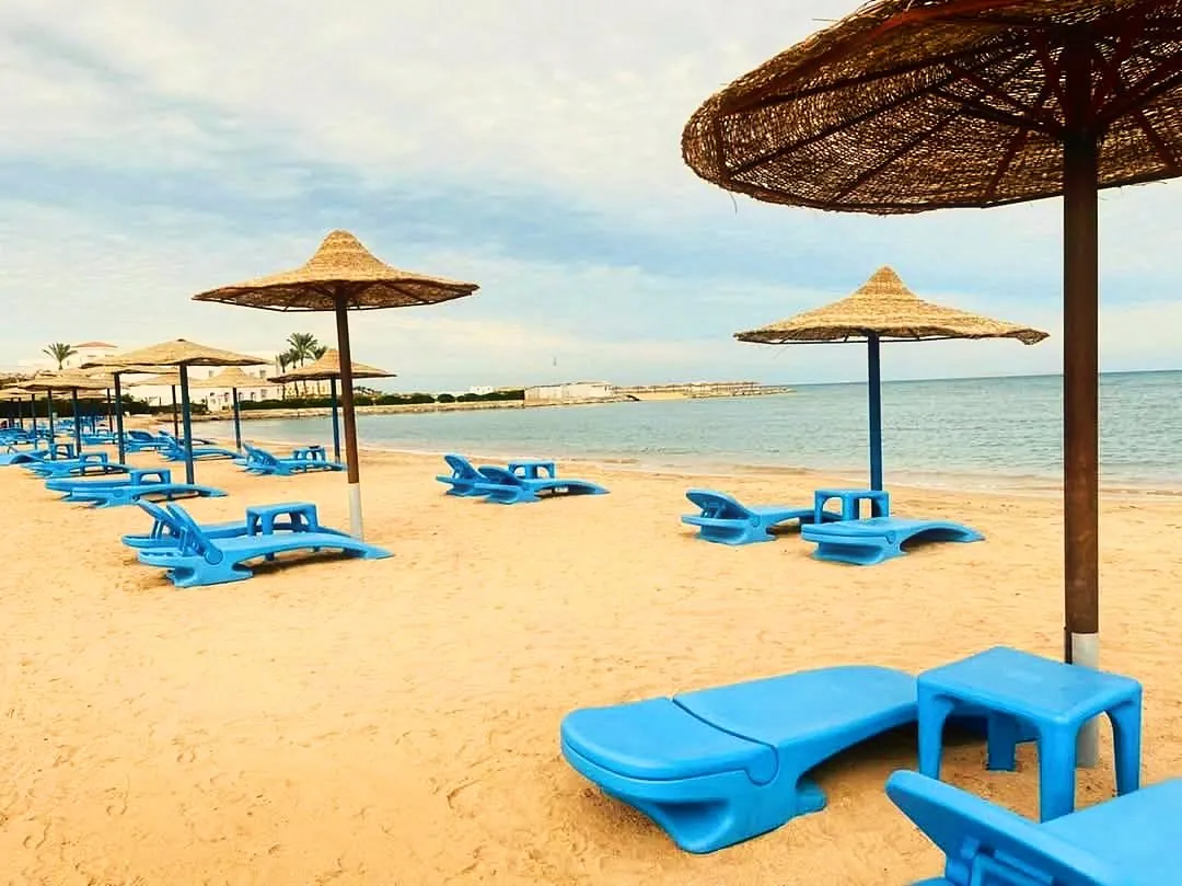 Strohschirme und blaue Sonnenliegen im Sand am Wasser