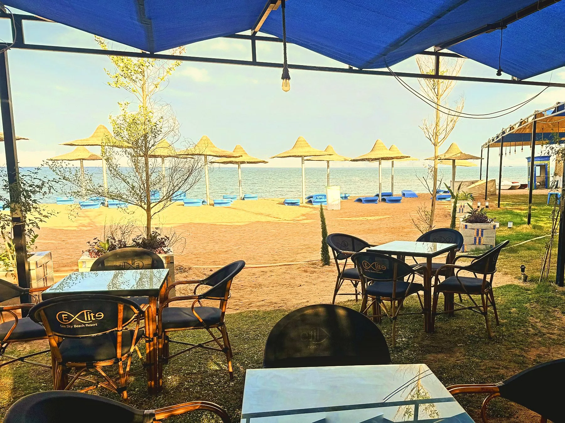 Das Strandcafé: Tische unter Sonnensegeln, Strohschirme und das Meer