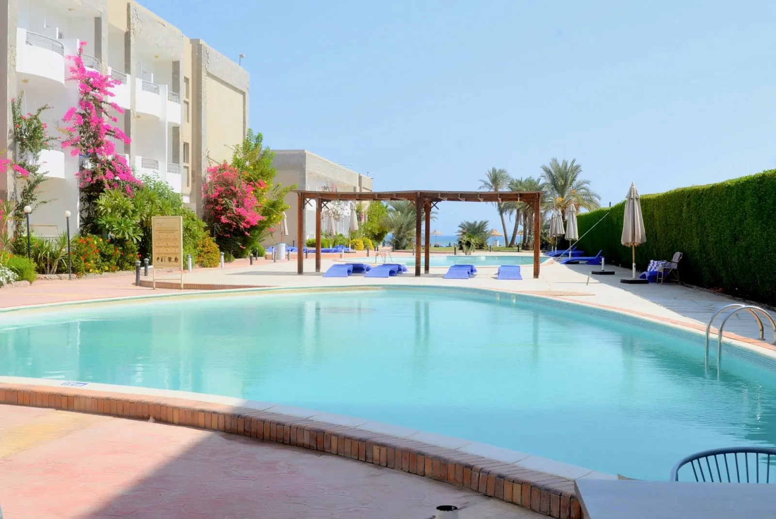 Ein Pool mit Palmen und rosa Bougainvillea zwischen den Gebäuden des Resorts