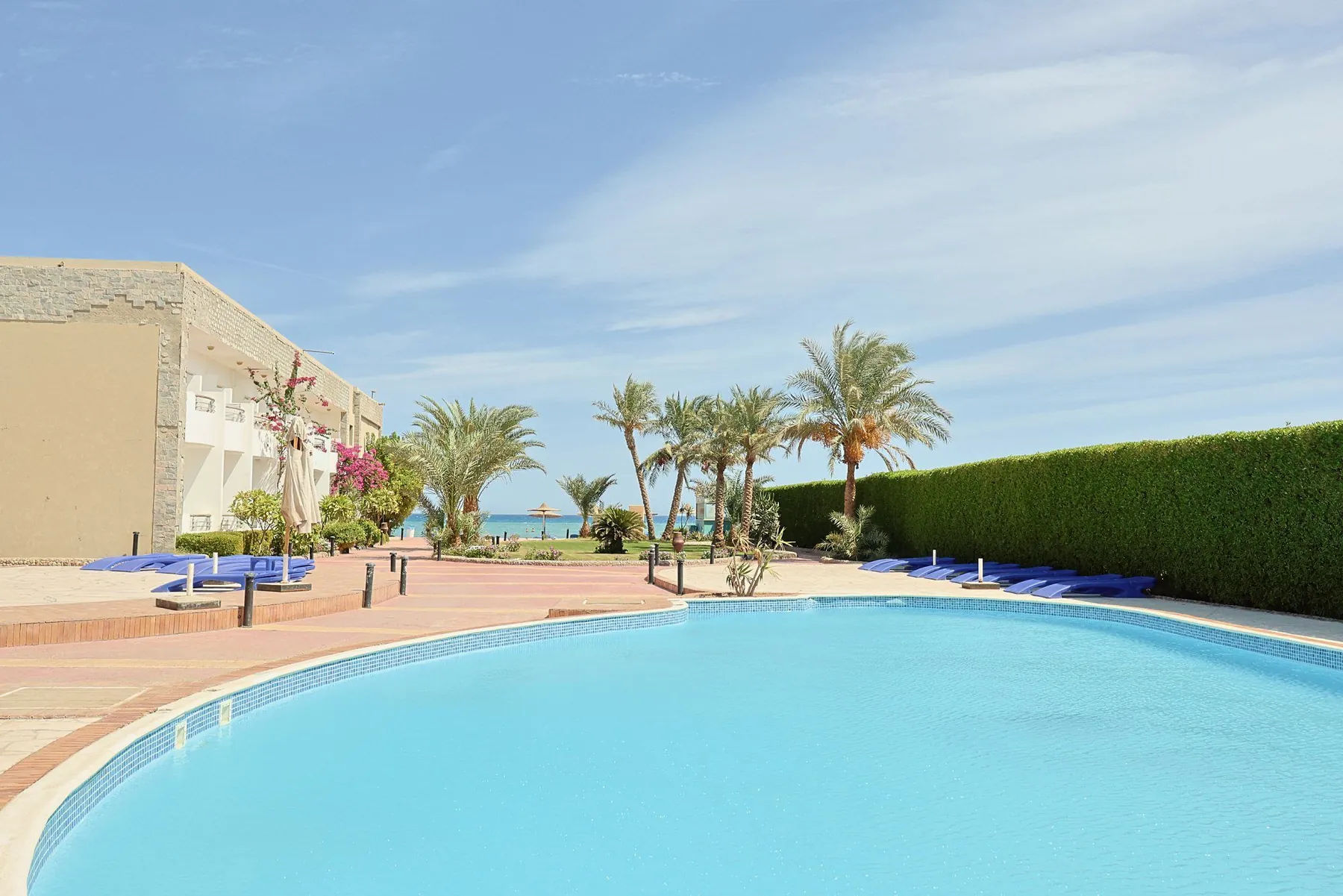 Ein ruhiger Pool mit Palmen, Sonnenliegen und dem Meer in der Ferne