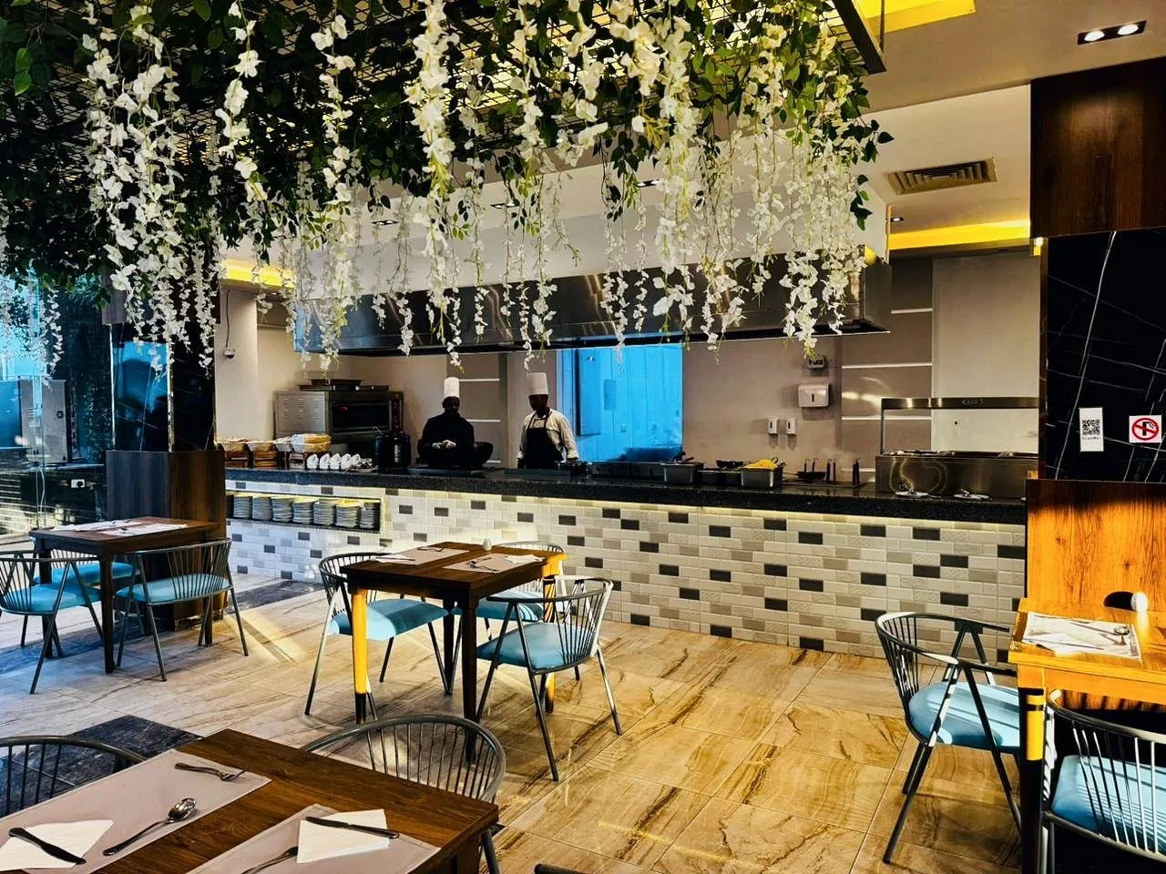 Die offene Küche und der Grill hinter dem Buffet, unter hängenden weißen Blumen